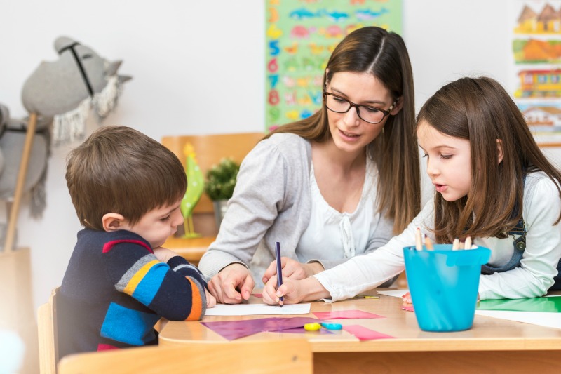 SMALL Brunette teacher with glasses and kids at table
